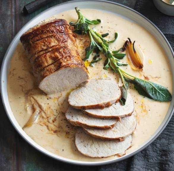 Braten aus Schweinefilet angeschnitten und angerichtet in Mascarpone-Sauce mit Salbeiblättern auf einer Servierplatte