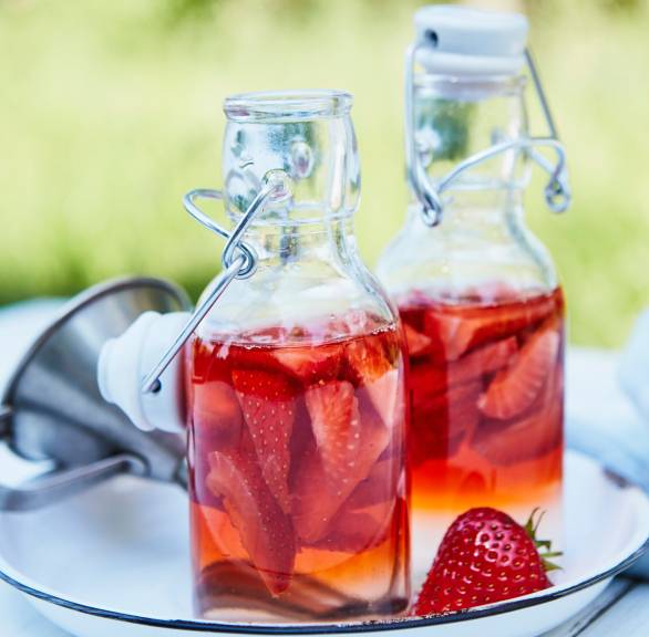 Selbst gemachter Erdbeeressig in zwei Henkelflaschen auf einem Holztisch im Garten