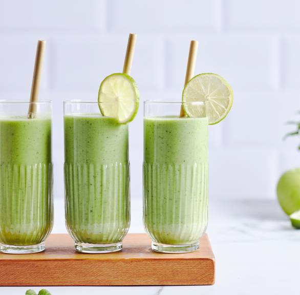 Grüner Smoothie in drei Gläsern auf einem Tisch mit Avocado, Gurke, Banane & Spinat