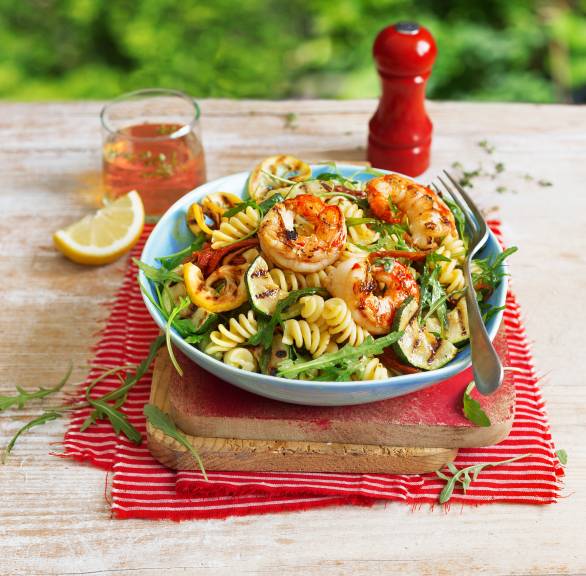 Nudelsalat mit gegrillter Zucchini und gegrillten Garnelen in einer Salatschüssel auf einem Tisch