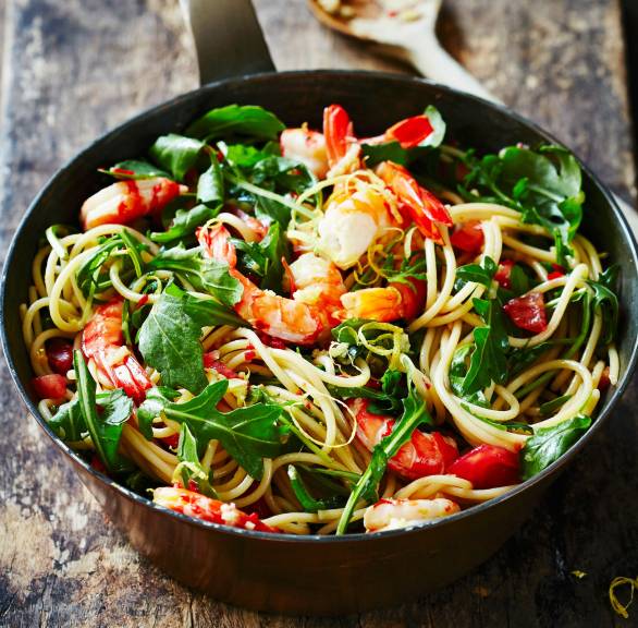 Spaghetti mit Garnelen, Rucola und Zitrone in einer gusseisernen Pfanne auf einem Holztisch