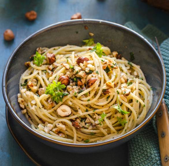 Spaghetti mit Haselnusspesto getoppt von Haselnusskernen und frischer Petersilie auf einem tiefen Pastateller