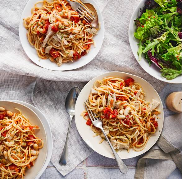 Drei Teller mit Thunfisch, Bohnen und frischen Kirschtomaten angerichtet auf einem Tisch, daneben eine Salatschüssel