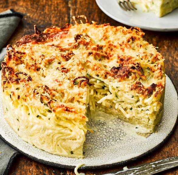 Runder Spaghettikuchen mit Sauce aus drei Käsesorten angeschnitten auf einem Teller