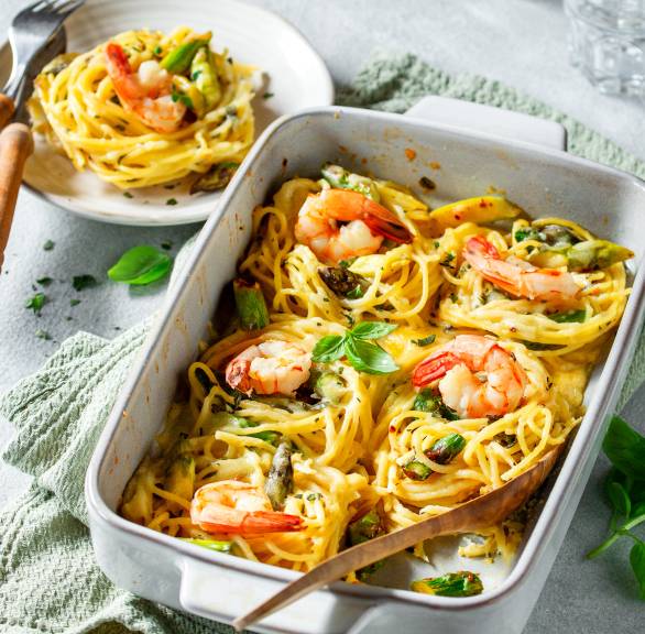 Auflaufform mit Sparhettinestern, grünen Spargelstücken und Garnelen auf einem Tisch