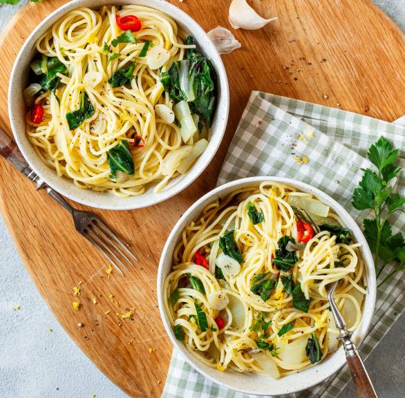 Zwei Portionen Spaghettini aglio e olio mit Mangold von oben auf einem Holzbrett