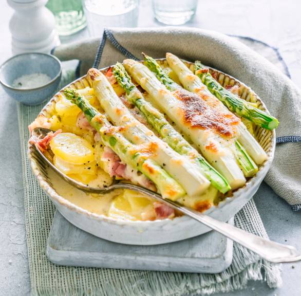 Kartoffelgratin mit Spargel, Schinken und Mozzarella in einer Auflaufform auf einem Tisch