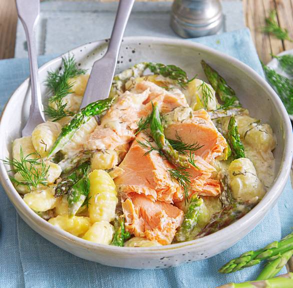 Auf dem Blech gebackene Gnocchi mit grünem Spargel und Lachsfilet in Sahnesauce auf einem tiefen Teller