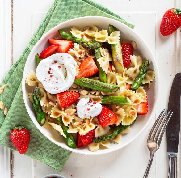 Spargelsalat mit Farfalle, Erdbeeren, Burrata und Pinienkernen in einer Schüssel auf einem Holztisch