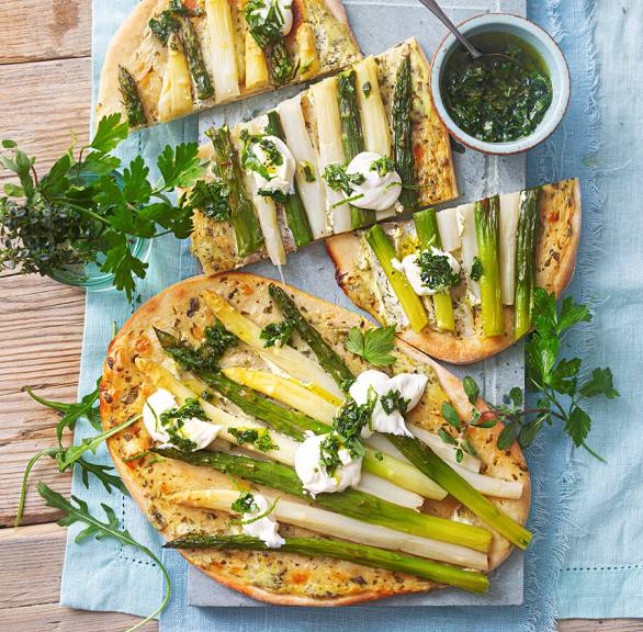 Spargelfladen aus Quark-Öl-Teig getoppt von Ziegenfrischkäse-Creme in Streifen geschnitten auf einem Holzbrett