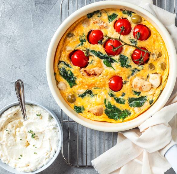  Frittata mit Hähnchen, Tomaten und Spinat in einer ofenfesten Pfanne, daneben  Feta-Dip