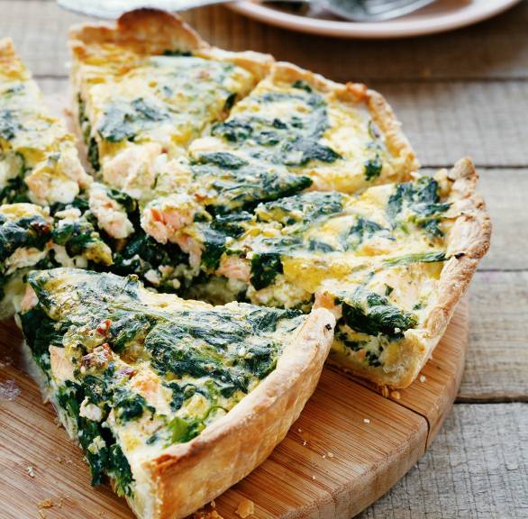 Lachs-Spinat-Quiche angeschnitten auf einem Holzbrett