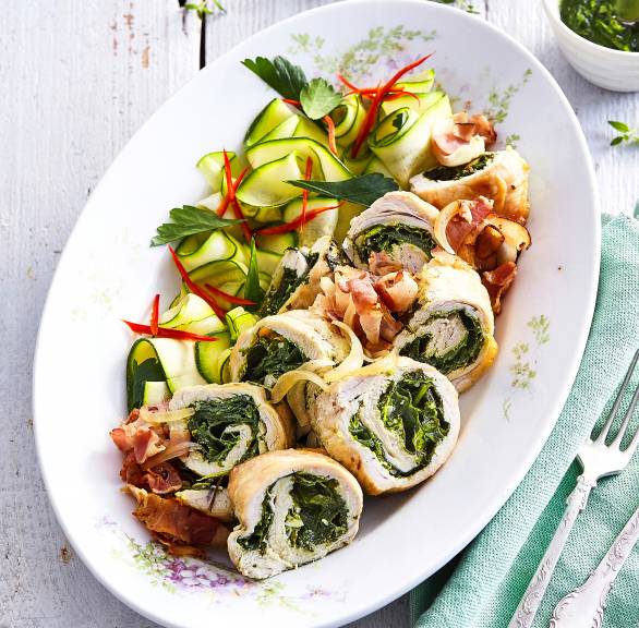 Puteninvoltini mit Spinatfüllung angerichtet neben Zucchinisalat, getoppt von Pancetta und Pesto auf einer Servierplatte