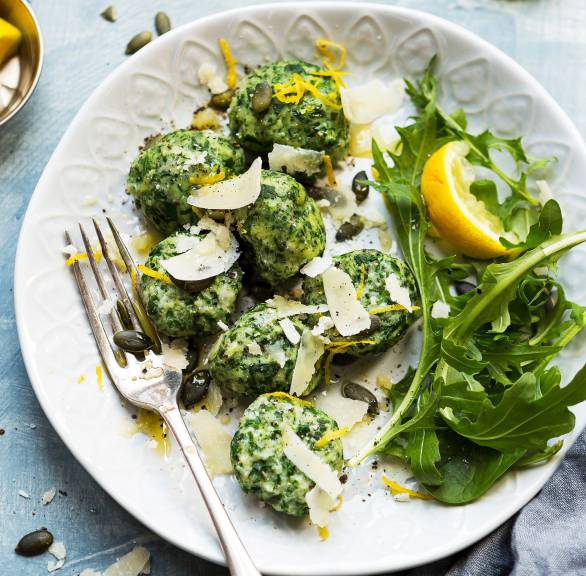 Selbstgemachte Spinat-Ricotta-Gnudi angerichtet auf Rucola mit Kürbiskernen und Parmesan auf einem Teller