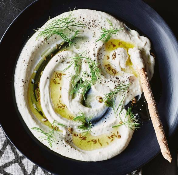 Stockfischpüree in einer Schale getoppt mit Fenchelöl, daneben Grissini in einem Glas auf einem Tisch