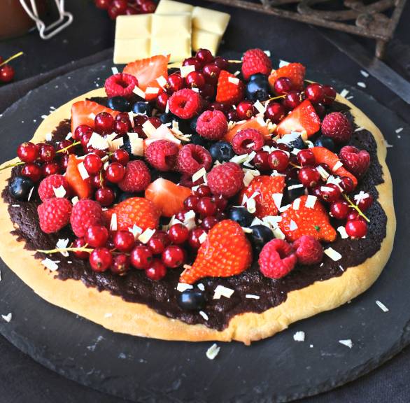 Süße Schokopizza mit frischen Beeren und weißen Schokoladenraspeln getoppt auf einer Schieferplatte