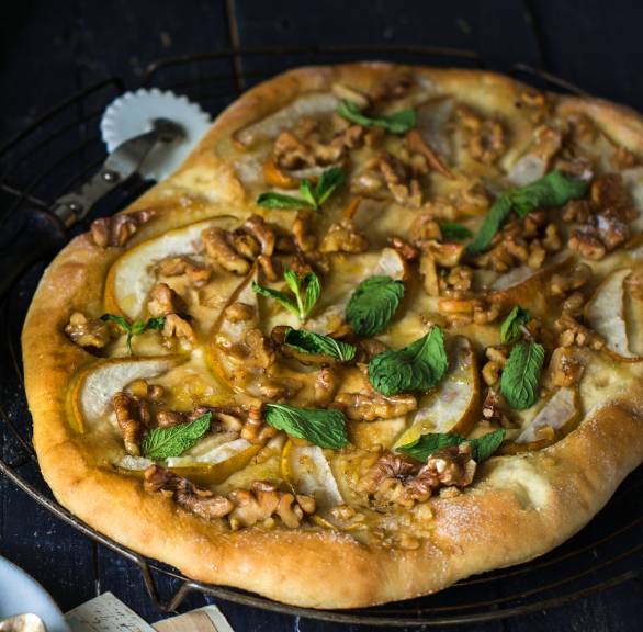 Selbstgebackene süße Honig-Focaccia belegt mit Birne und Walnuss getoppt von Minzblättern auf einer Servierplatte