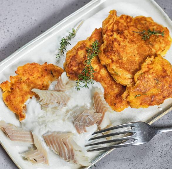 Süßkartoffel- Pfannkuchen auf einem Teller getoppt mit Parmesancreme, darauf Forellenfiletstücke