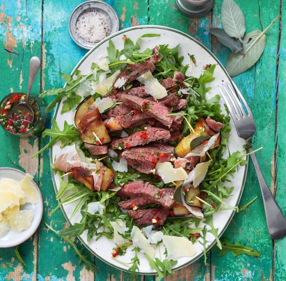 Teller mit Rindfleischstreifen und Auberginenröllchen auf einem Salatbett