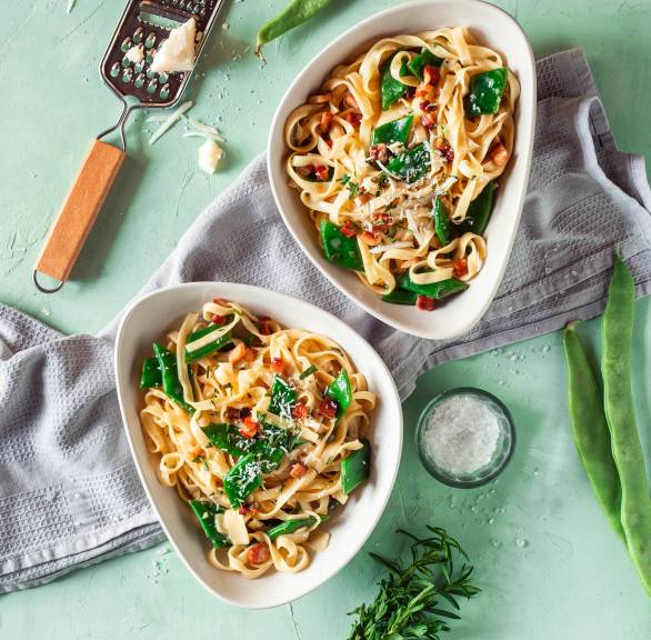 Tagliatelle mit Carbonara mit grünen Bohnen angerichtet auf zwei Pastatellern