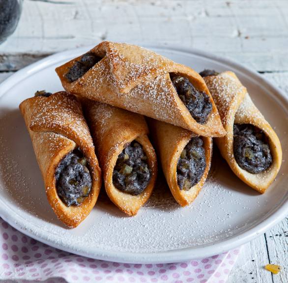 Fünf selbstgebackene Cannoli mit Mohn-Ricotta-Füllung gestapelt auf einem Dessertteller