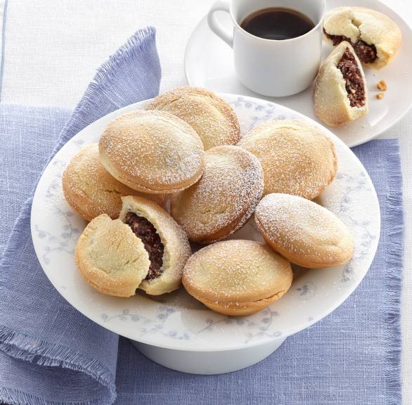 Bocconotti alle mandorle e cacao Teigtaschen mit Mandel-Kakao-Füllung auf einer Platte, schokoladige Füllung gut sichtbar, daneben eine Tasse Kaffee