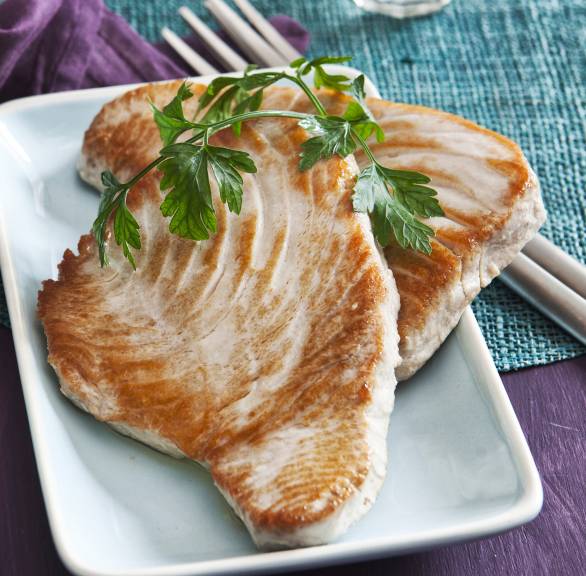 Zwei gebratene Thunfischsteaks auf einem rechteckigen Teller, daneben eine Schale mit rotem Pesto