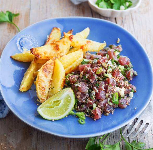 Thunfisch-Tartar angerichtet auf einem Teller, daneben Parmesankartoffelspalten, Limette und Petersilie