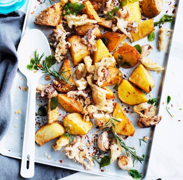 Tintenfisch und Kartoffeln aus dem Ofen auf einem Backblech, daneben ein Teller und eine Wasserflasche