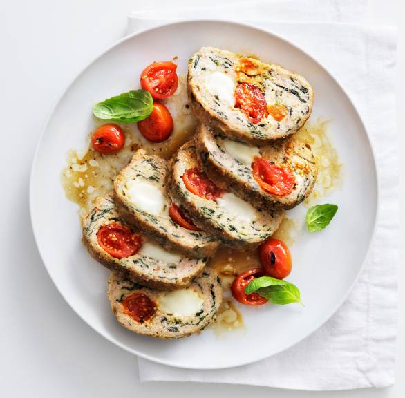 Mehrere Scheiben von gebackenem Putenhackbraten mit Tomaten-Mozzarella-Füllung angerichtet auf einer Servierplatte