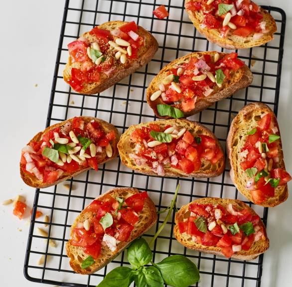 Geröstete Ciabattascheiben belegt mit Tomaten, Zwiebeln, Pinienkernen und Basilikum auf einem Backgitter
