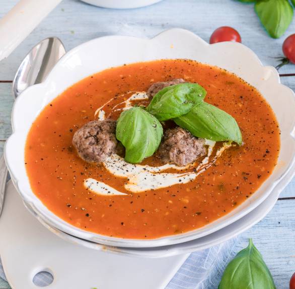 Italienische Tomatensuppe und einem Topf und in einem Suppenteller getoppt mit Hackbällchen, Crème fraîche und Basilikum