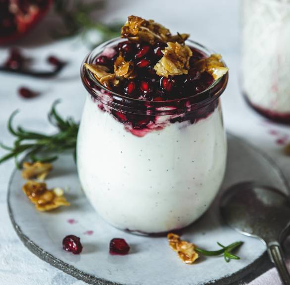 Vanillecreme in Gläsern getoppt mit Granatapfelsoße und Mandelkkrokant auf einem Tisch