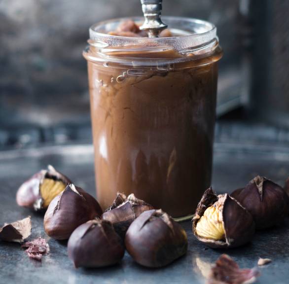 Selbstgemachter veganer süßer Maronenaufstrich in einem Weckglas auf eniem Tisch, daneben geröstete Maronen