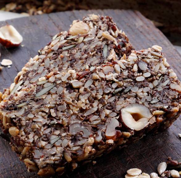 Vollkornbrot in Scheiben auf einem Holzbrett, daneben Nüsse