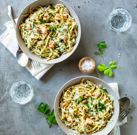 Vollkornnudeln mit Lachs und cremiger Sauce getoppt von frischen Kräutern in einem tiefen Teller