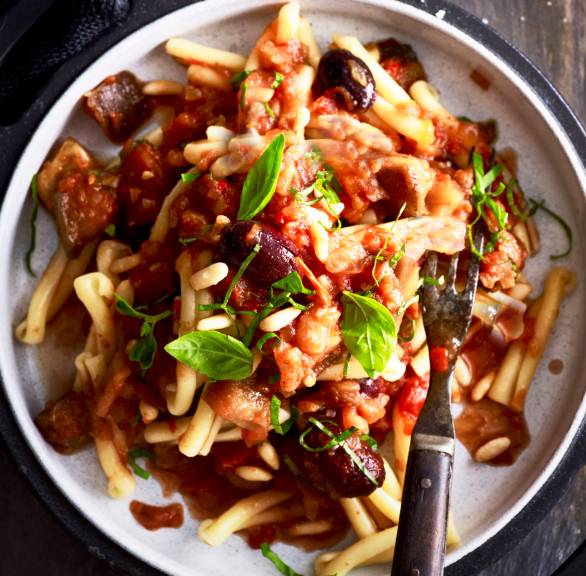 Vollkorn-Dinkelnudeln mit Sauce, Auberginen, Oliven und Pinienkernen angerichtet auf einem Teller