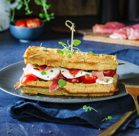Doppelte Parmesan-Buttermilchwaffelbelegte mit Tomate, Mozzarella und Parmaschinken angerichtet auf einem Teller