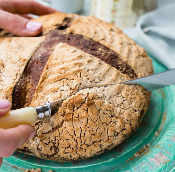 Rundes Walnussbrot auf einem Teller, das gerade angeschnitten wird