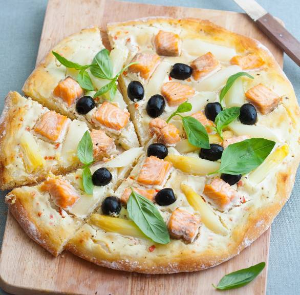 Runde Spargelpizza mit Lachs auf einem Holzbrett in Pizzastücke geschnitten