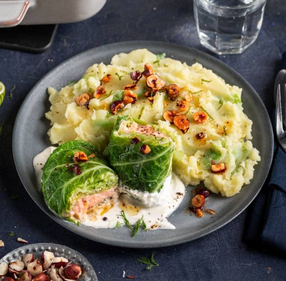 Wirsing-Lachs-Involtini mit Kartoffelstampf und Haselnussbutter angerichtet auf einem Teller