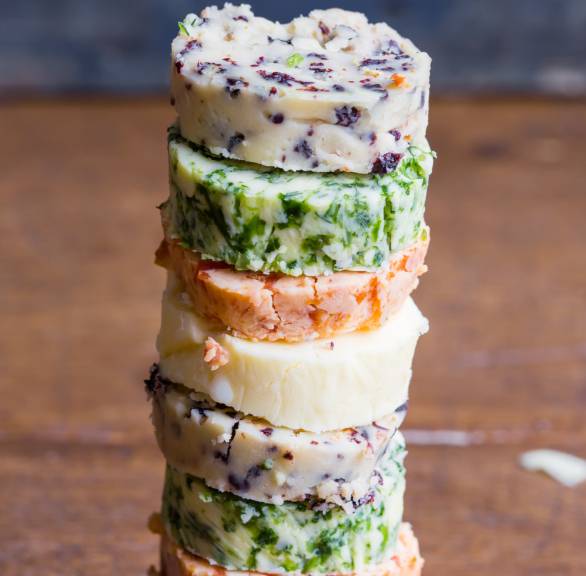 Verschiedene Stücke selbstgemachter Würzbutter-Rollen gestapelt auf einem Holzbrett