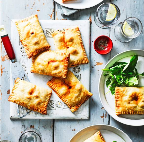 Mehrere gebackene, vegetarisch gefüllte Pizzataschen auf Tellern auf einem Tisch, daneben Salat