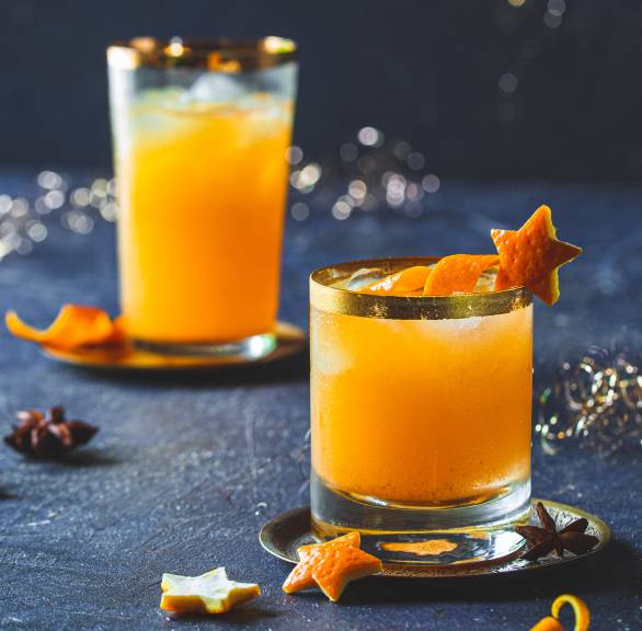 Orangen-Gin-Cocktail mit Weihnachtsgewürzen in zwei Longdrinkgläsern garniert mir Sternen aus Orangenschale auf einem festlich dekorieren Tisch