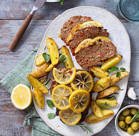 Hackbraten angeschnitten auf einer Servierplatte mit Rosmarinkartoffeln und gebackenen Zitronenscheiben