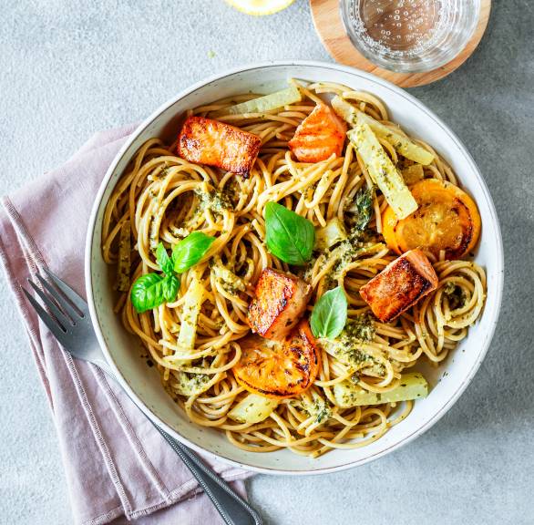 Vollkornspaghetti mit gebratenen Lachsfiletstücken und Zitronen-Sahnesoße getoppt von frischem Basilikum auf einem Pastateller