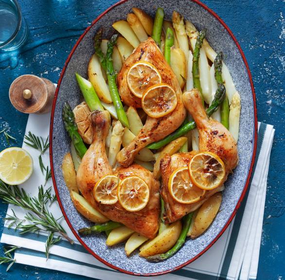 Gebackene Hähnchenkeulen mit Kartoffelspalten, grünem und weißem Spargel angerichtet auf einer Servierplatte