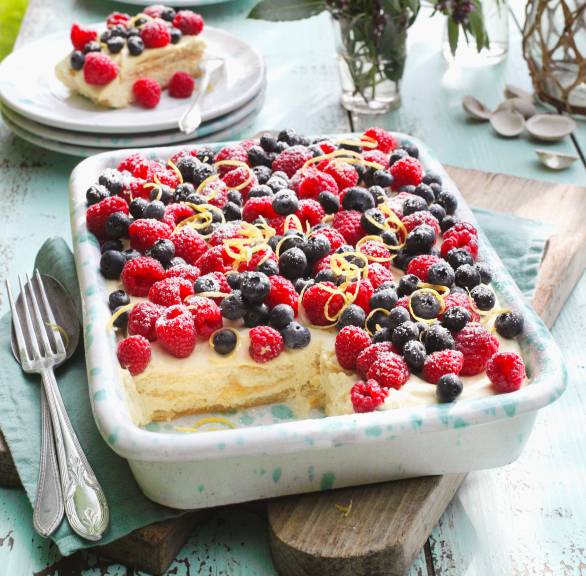 Zitronentiramisu angeschnitten in einer Auflaufform garniert mit verschiedenen Beeren auf einem Tisch im Grünen