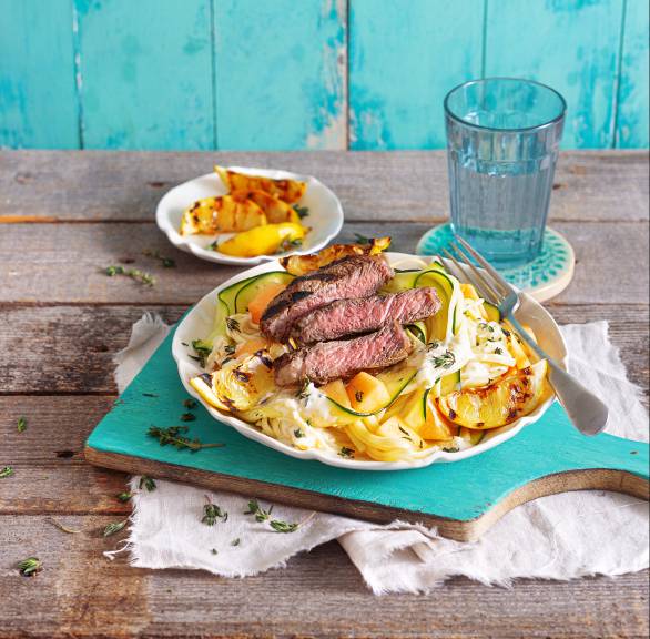 Linguine und Zucchini auf einem Teller, darauf gegrilltes Steak und Melonenstücke