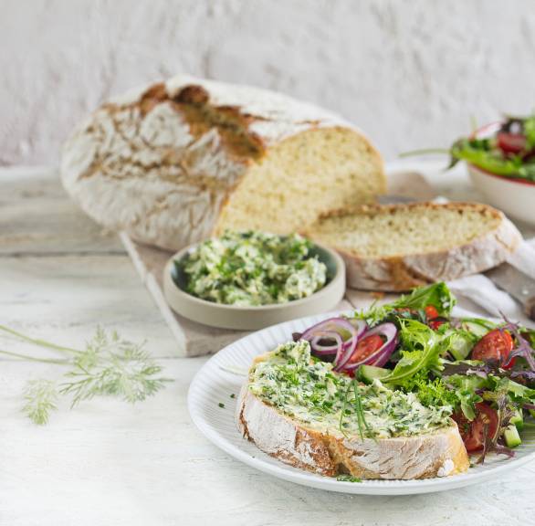 Zucchinibrot angeschnitten auf einem Tisch, einige Scheiben serviert auf einem Teller mit Salat und Aufstrich